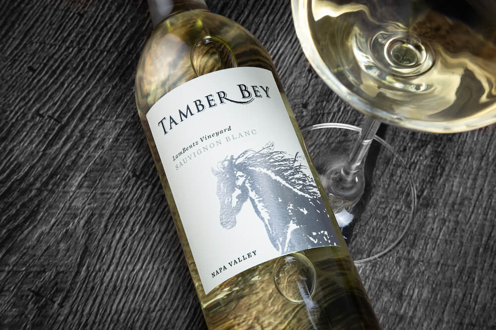 bottle of sauvignon blanc lying on a gray wood table with a glass of white wine partially visible.